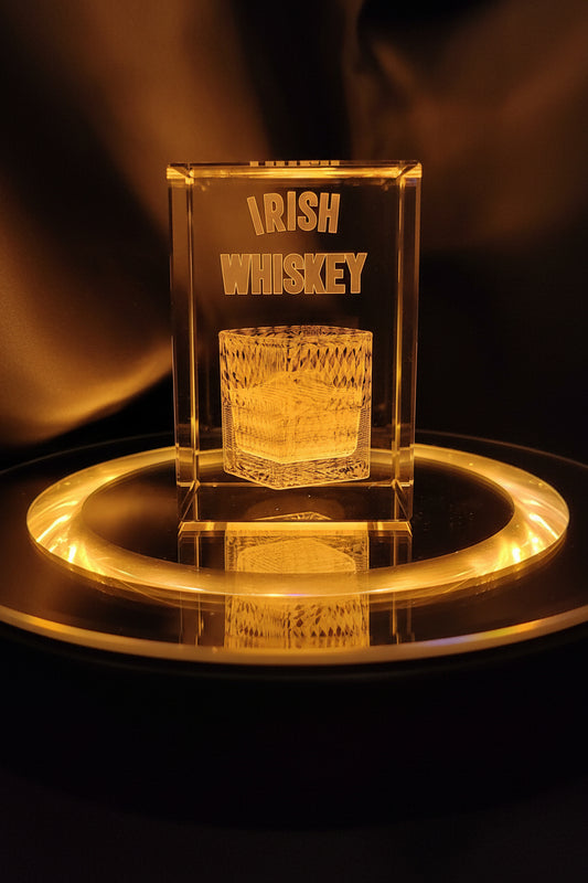 A clear glass whiskey decanter with 'IRISH WHISKEY' text, displayed on a reflective surface with a blurred background.